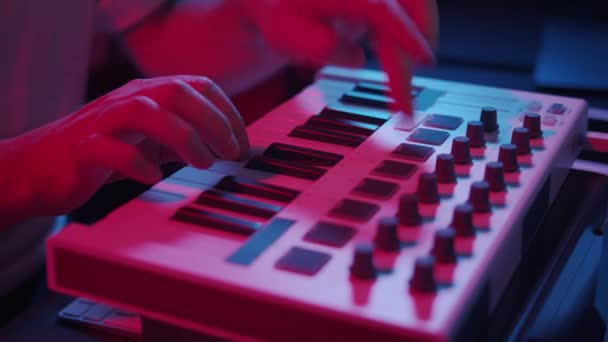 Mãos masculinas gravando música usando teclado midi em estúdio em casa, luzes de néon — Vídeo de Stock