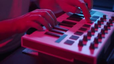 Erkek eller evdeki stüdyoda Midi klavyesiyle müzik kaydediyor, neon ışıklar.