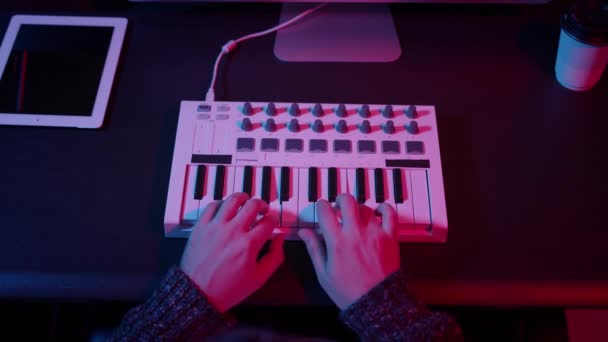 Vista dall'alto delle mani utilizzando la tastiera midi in studio domestico con luci al neon — Video Stock