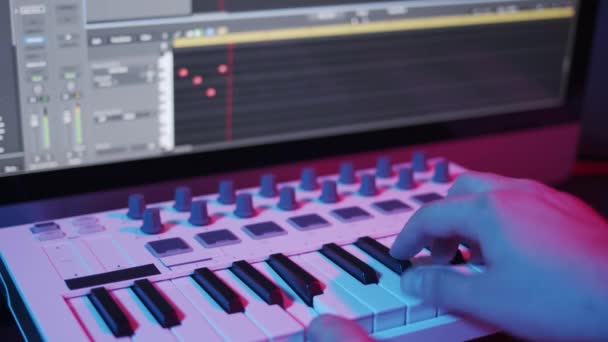 Manos masculinas grabando teclado midi en secuenciador en el estudio en casa, luces de neón — Vídeos de Stock