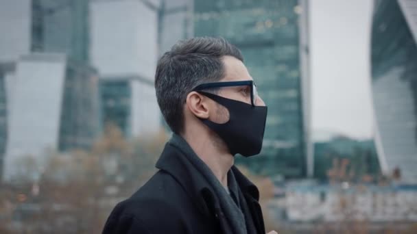 Üzletember védő maszk séta a háttér felhőkarcolók — Stock videók