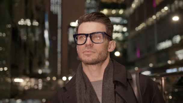 穿着外套和眼镜的商人，晚上在商业楼的背景下 — 图库视频影像