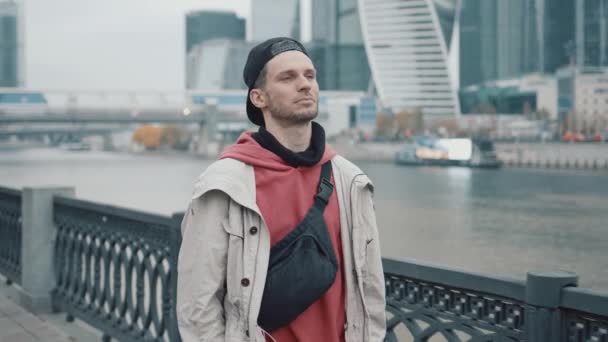 Pria berjalan di atas latar belakang pencakar langit bisnis dengan hoodie merah — Stok Video