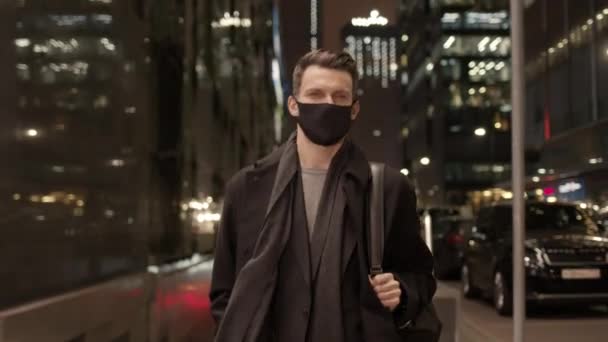 Hombre en máscara protectora caminando sobre el fondo de edificios de vidrio en la noche — Vídeo de stock