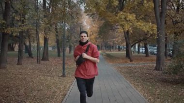 Şehirdeki sonbahar parkında spor giyim alanında koşan bir adam.