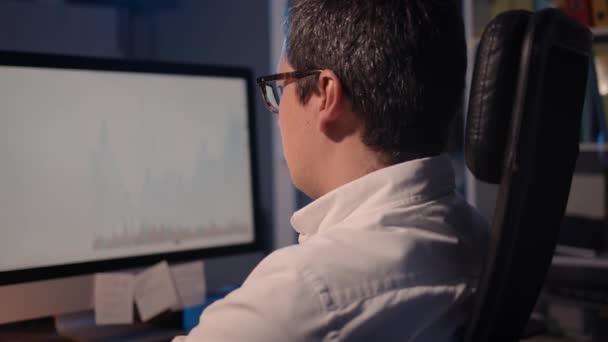 Человек трейдер смотрит на экран с графиками фондового рынка, домашний офис — стоковое видео