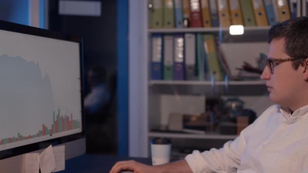 Чоловік трейдер дивиться на екран з графіками фондового ринку, домашній офіс — стокове відео