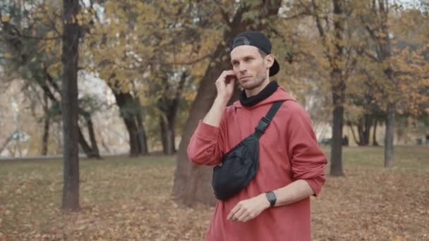 Man runner put on earbuds and tap on smartwatch in city park get ready for running — Stock Video