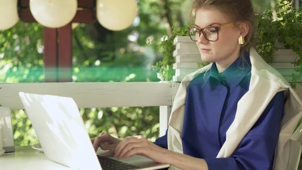 Yeşil ağaçların arka planında dizüstü bilgisayarı olan gözlüklü genç bir kadın. — Stok fotoğraf