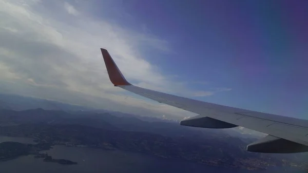 Ala di un aereo che vola sopra le nuvole serali e la superficie della città — Foto Stock