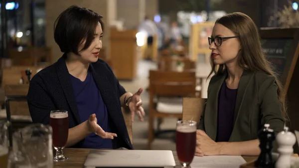 Dos amigas rubias y morenas discutiendo planes sentadas en un bar — Foto de Stock