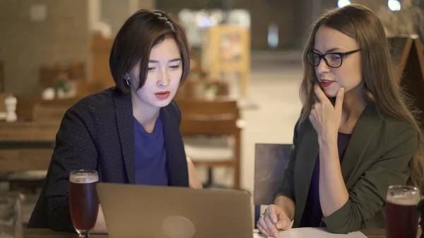 Duas mulheres loiras e morenas amigas discutindo planos com laptop no bar — Fotografia de Stock