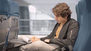 Genç adam trende notlar almakla meşgul, banliyö treninde yalnız genç bir adam.