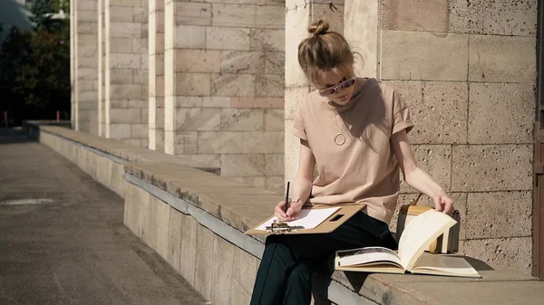 Young woman in sunglasses preparing for the exam outside