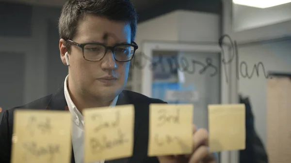 Jeune patron homme d'affaires écrit des plans sur les notes collantes sur le mur de verre — Photo