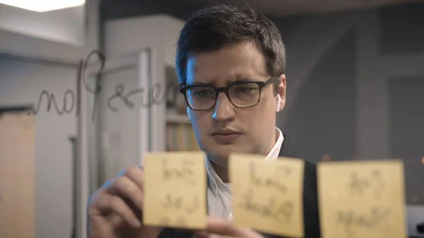 Giovane uomo d'affari capo scrivere piani sulle note appiccicose sulla parete di vetro — Foto Stock