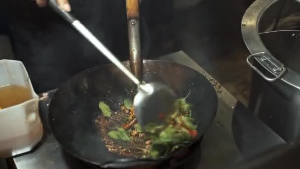 Cook omrörning bönor med gröna blad på en svart gjutjärn pan — Stockvideo