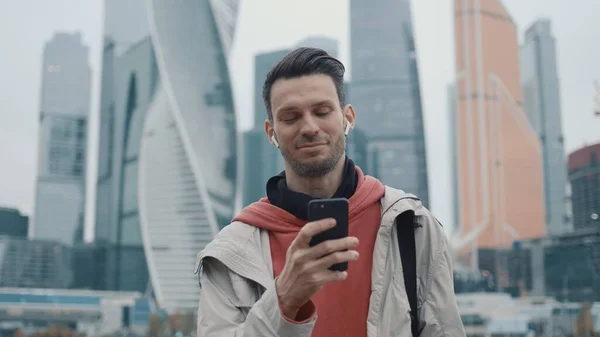 Uomo in felpa rossa scorrendo il telefono sullo sfondo dei grattacieli — Foto Stock