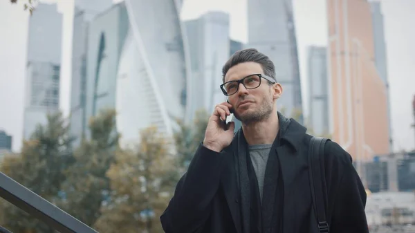 Uomo in cappotto che parla al telefono su sfondo di grattacieli in giorno di autunno — Foto Stock