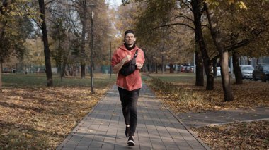 Şehirdeki sonbahar parkında spor giyim alanında koşan bir adam.