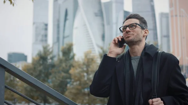 Uomo in cappotto che parla al telefono su sfondo di grattacieli in giorno di autunno — Foto Stock