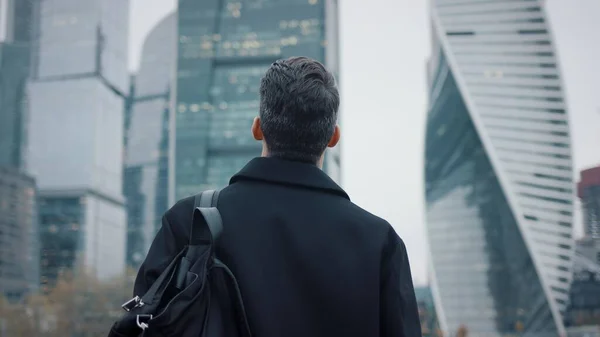 Hombre de abrigo caminando hacia edificios de negocios, rascacielos de cámara lenta — Foto de Stock