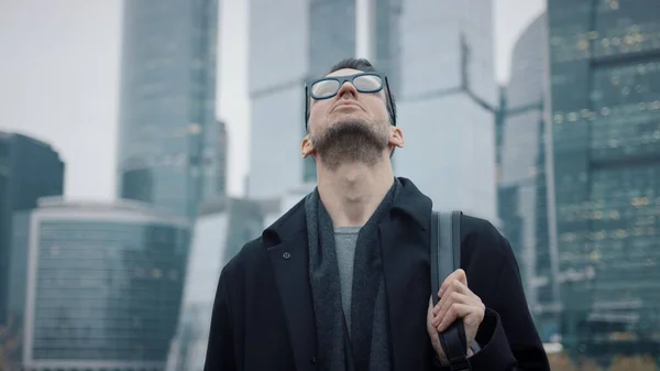 Uomo d'affari in cappotto nero guardando verso il cielo sullo sfondo di grattacieli — Foto Stock