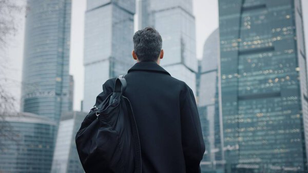 Businessman looking at the skyscrapers autumn day, black coat with eyeglasses