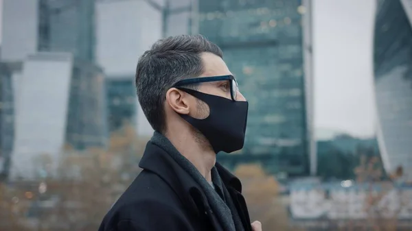 Empresario en máscara protectora caminar sobre fondo de rascacielos — Foto de Stock