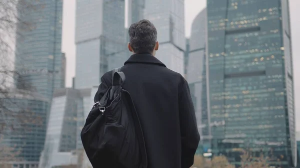Hombre de abrigo caminando hacia edificios de negocios, rascacielos de cámara lenta — Foto de Stock