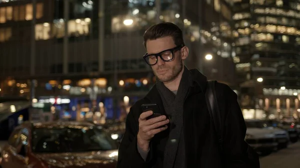 Hombre en gafas con teléfono en el fondo del edificio de negocios en la noche — Foto de Stock