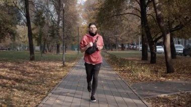 Şehirdeki sonbahar parkında spor giyim alanında koşan bir adam.