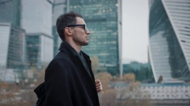 Siyah ceketli bir işadamı gökdelenlerin arka planında yürüyor