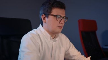 Geceleri ofiste beyaz gömlekle çalışan bir adam, ekrana bakıyor.