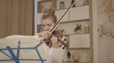 Genç sarışın kadın lüks bir evde keman çalıyor.