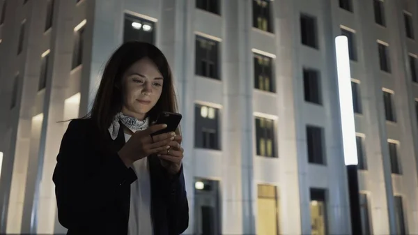 Vrouw alleen met een telefoon dragen zwarte jas en nek sjaal, nacht schot — Stockfoto