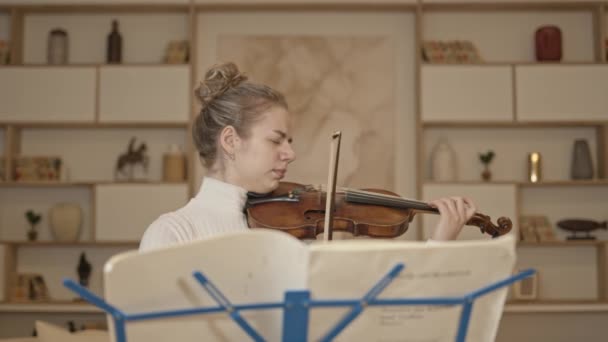 Giovane donna bionda che suona il violino con musica stand a casa sfondo interno — Video Stock