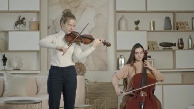 Lüks ev iç mekanında keman ve çello çalan bir dizi kadın.