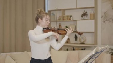 Genç sarışın kadın lüks bir evde keman çalıyor.