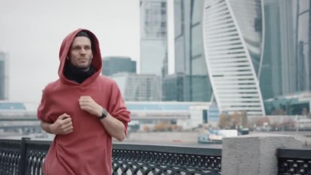 Man runner op de achtergrond van het bedrijfsleven wolkenkrabbers in rood hoodie — Stockvideo
