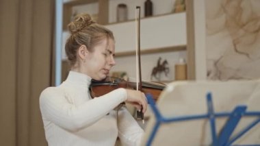 Genç sarışın kadın lüks bir evde keman çalıyor.