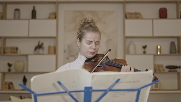 Jong blond vrouw spelen viool met muziek staan thuis interieur achtergrond — Stockvideo