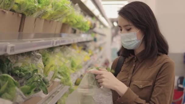 Młoda kobieta w masce ochronnej kupuje warzywa w sklepie spożywczym — Wideo stockowe