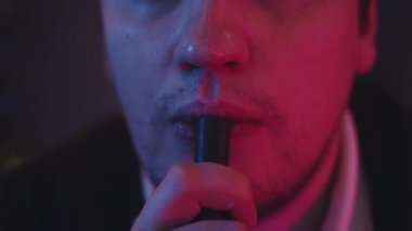 Erkek ağzı nargile içiyor, siyah arka planda hortum tutuyor.