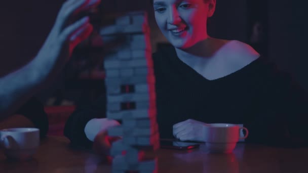 Gente jugando jenga en el bar nocturno con luces rojas y azules — Vídeos de Stock