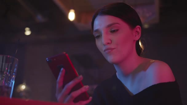 Kobieta z telefonem w ręku na tle wnętrza baru w neonach — Wideo stockowe
