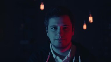 Gözlüklü ve kapüşonlu, koyu neon ışıklı bir adam.
