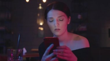 Elinde telefonu olan bir kadın barın arka planında neon ışıklarıyla.