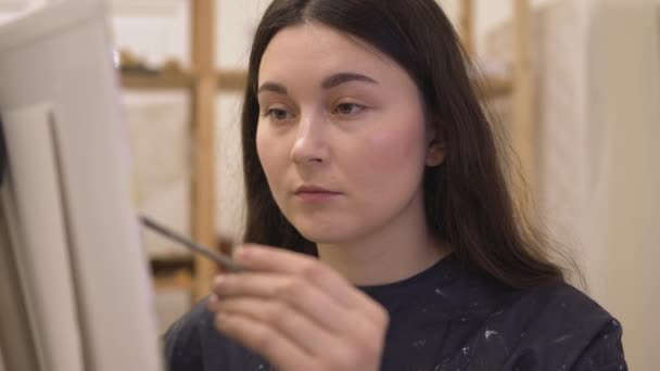 在现代艺术工作室工作的带画架的年轻女画家 — 图库视频影像