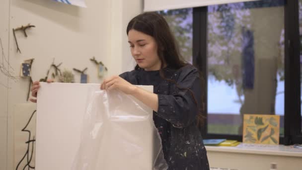 Ung kvinna artist packa upp ny duk i studio rum — Stockvideo